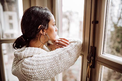 Young woman who is going through pregnancy alone looks out her window